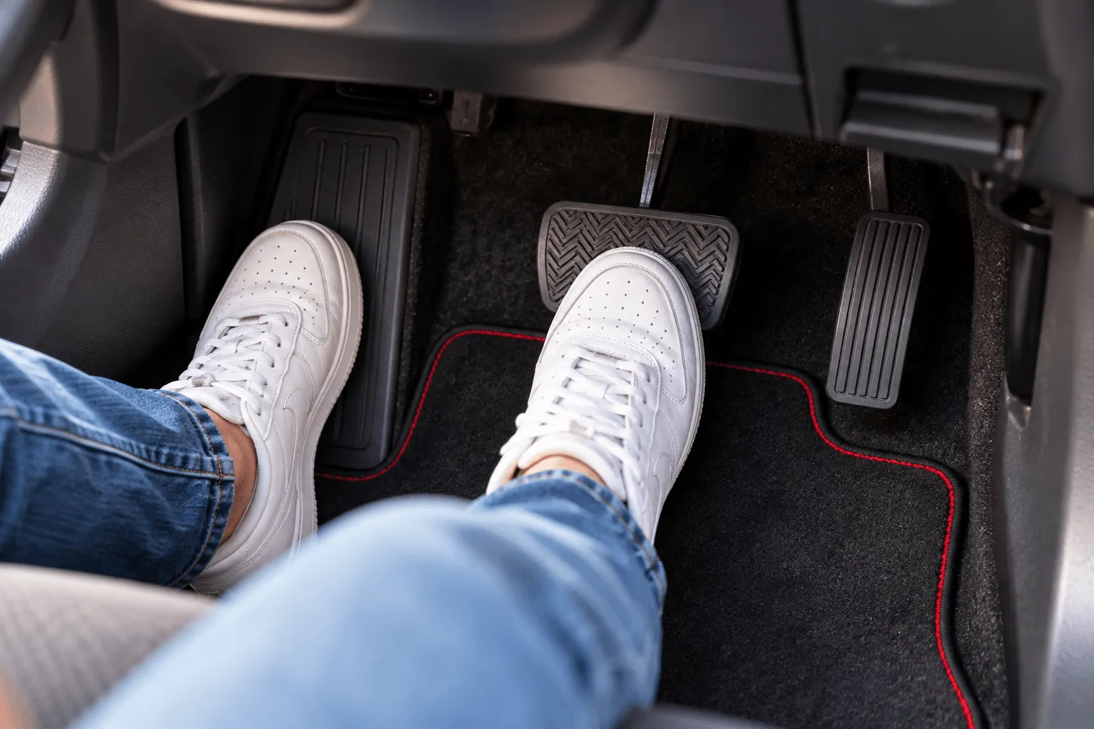 Learner in white trainers with both feet on the pedals in a car footwell